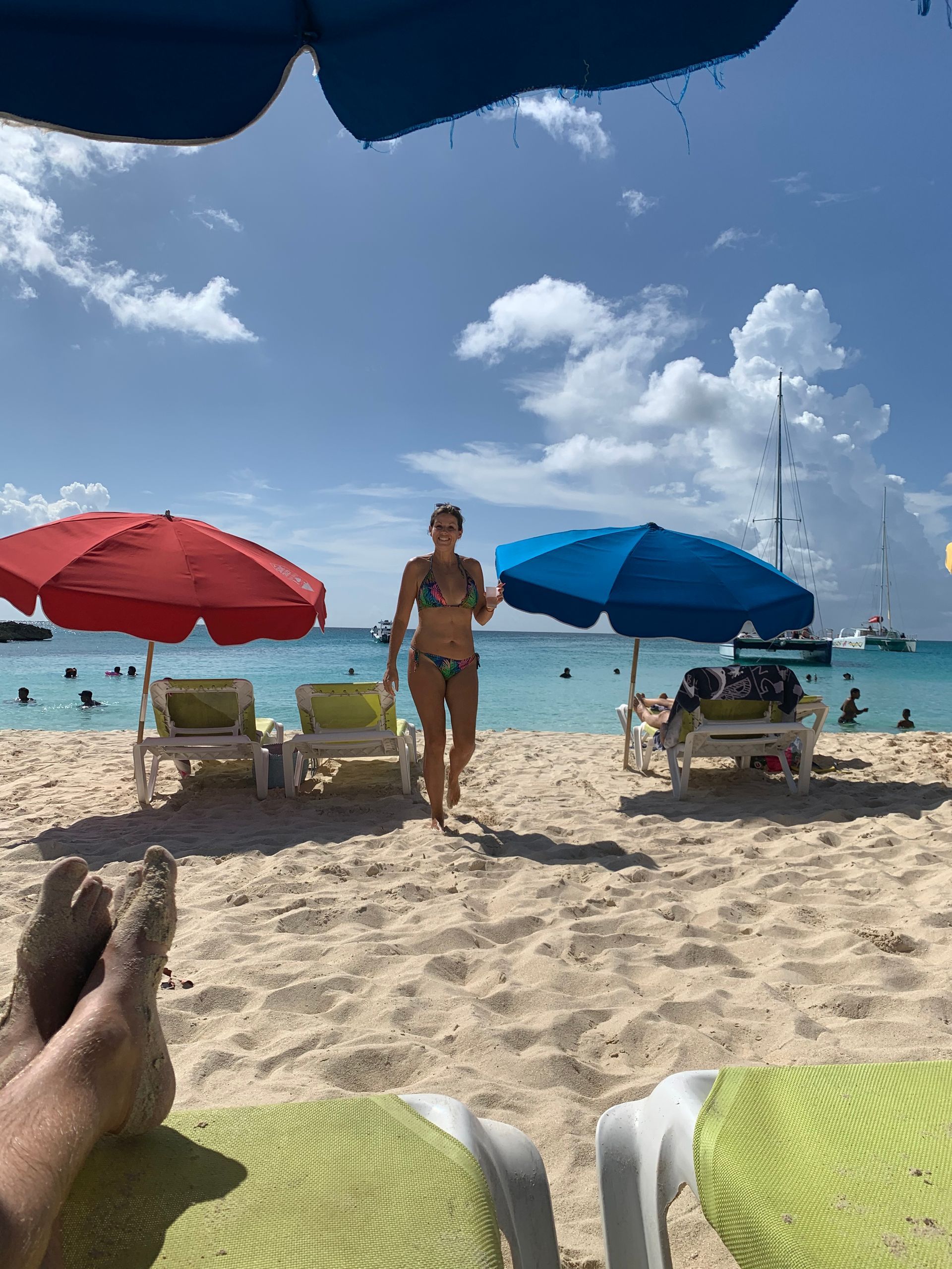 Woman in bikini walks on beach, between colorful umbrellas and lounge chairs. Blue sky.