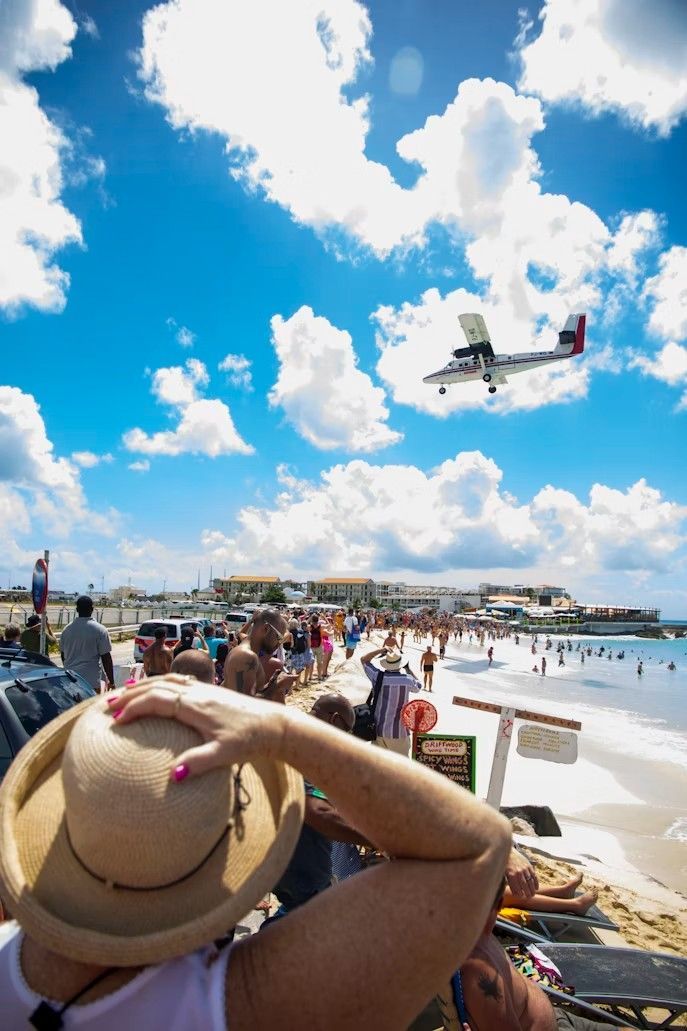 Beachgoers watch a low-flying airplane approach the runway against a blue sky.