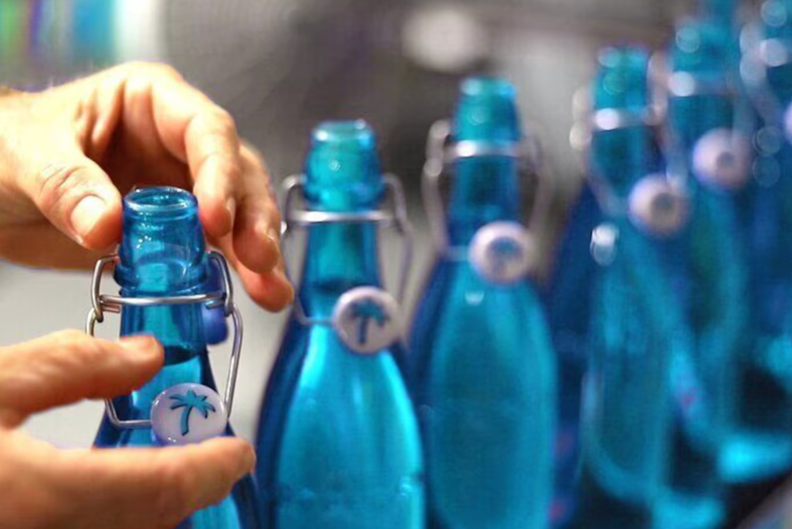 Person opening a blue glass bottle with a metal clasp, other bottles in the background.