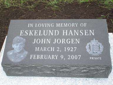 Gray gravestone with engraved memorial text and portrait, lying in grass