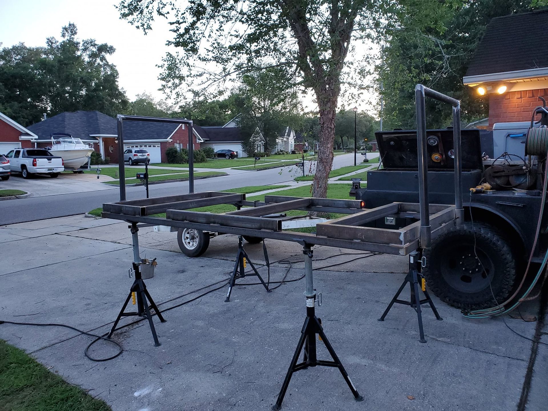 Trailer with a black motorcycle frame secured by ratchet straps in a driveway at dusk