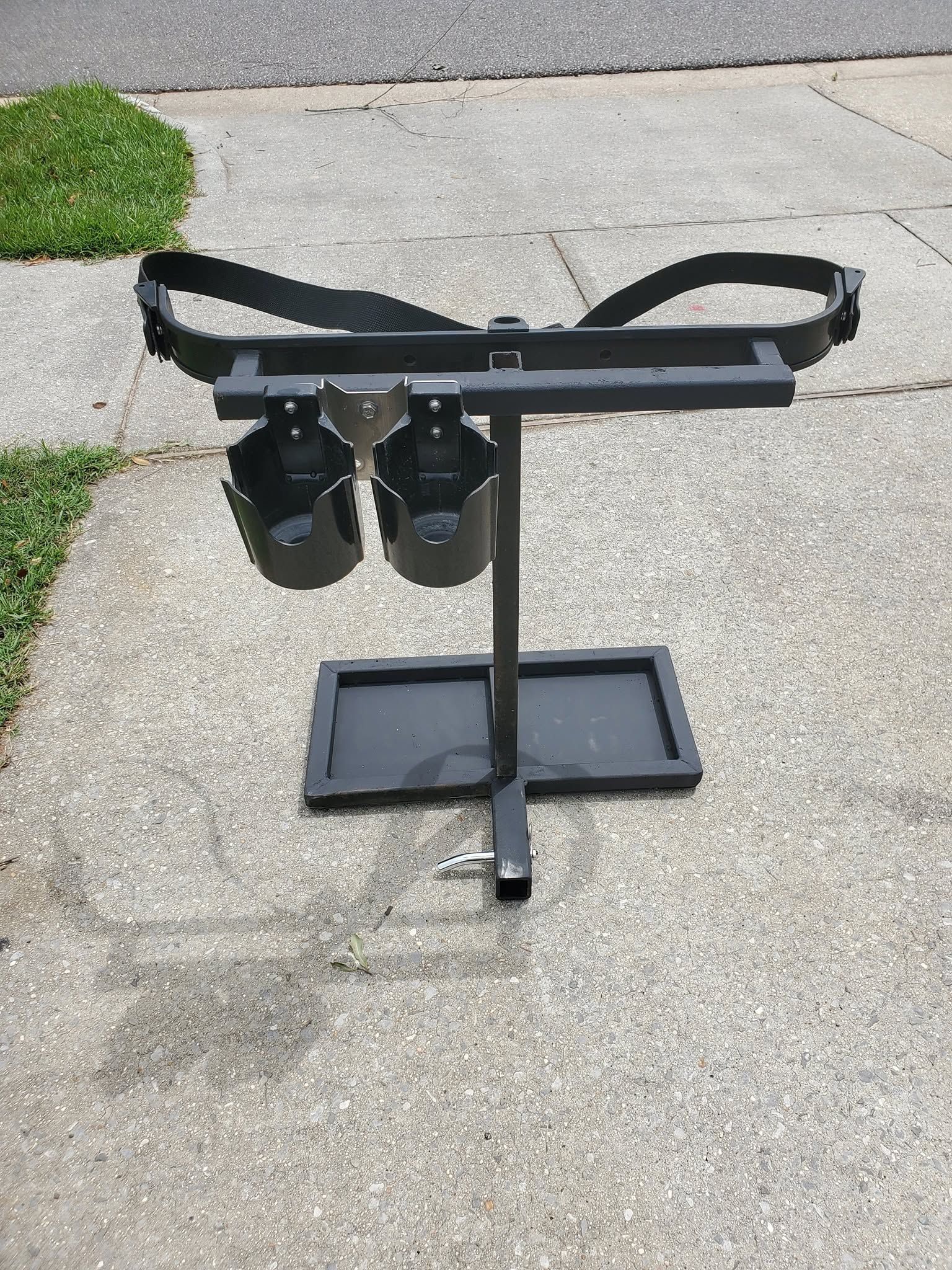 Black metal mobility walker stand with padded handles and footrests on a sidewalk near grass.
