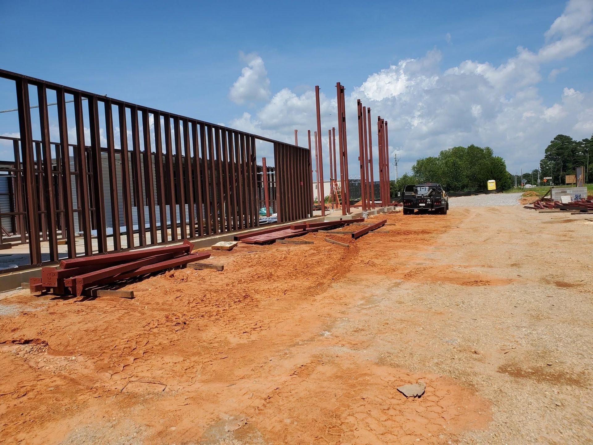 Construction site with steel framework along a dirt road under a cloudy sky