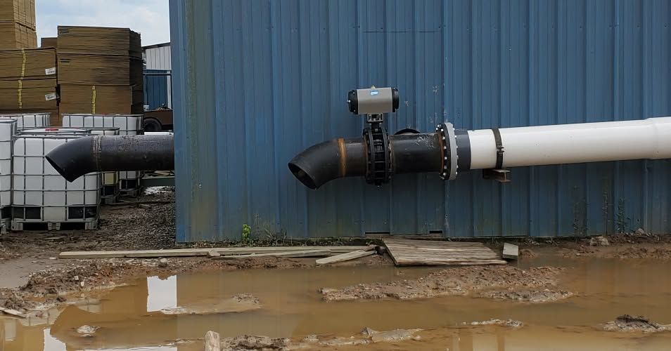 Industrial pipes and valves on a blue building beside muddy standing water