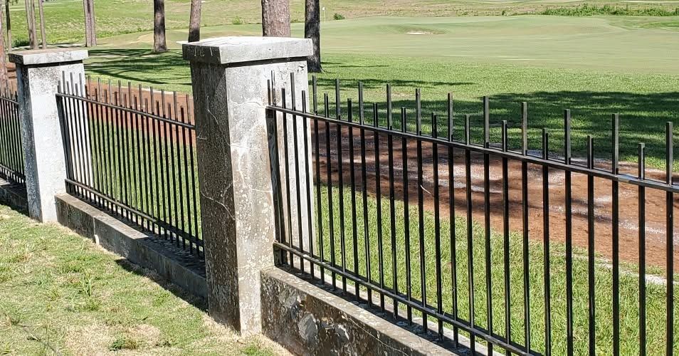 Black iron fence with stone pillars along a grassy park path beside a dirt road
