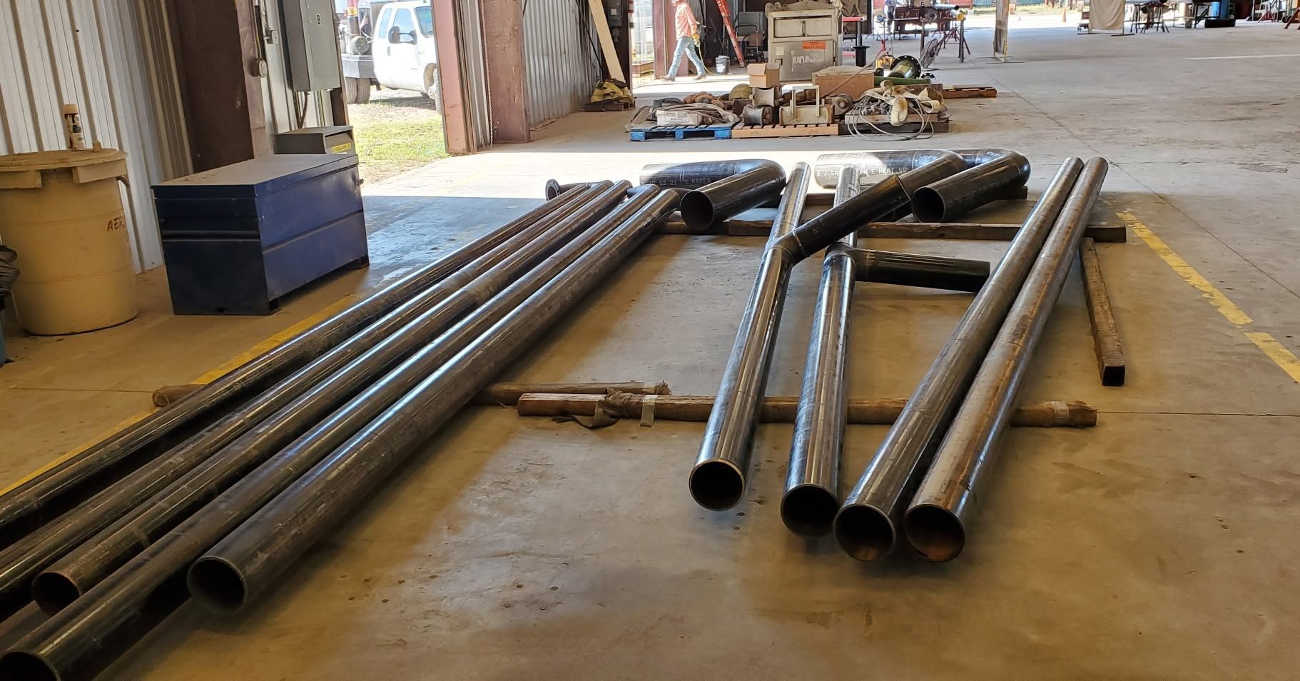 Steel pipes laid out on a warehouse floor, with long black tubes and shorter silver pipes in the background.