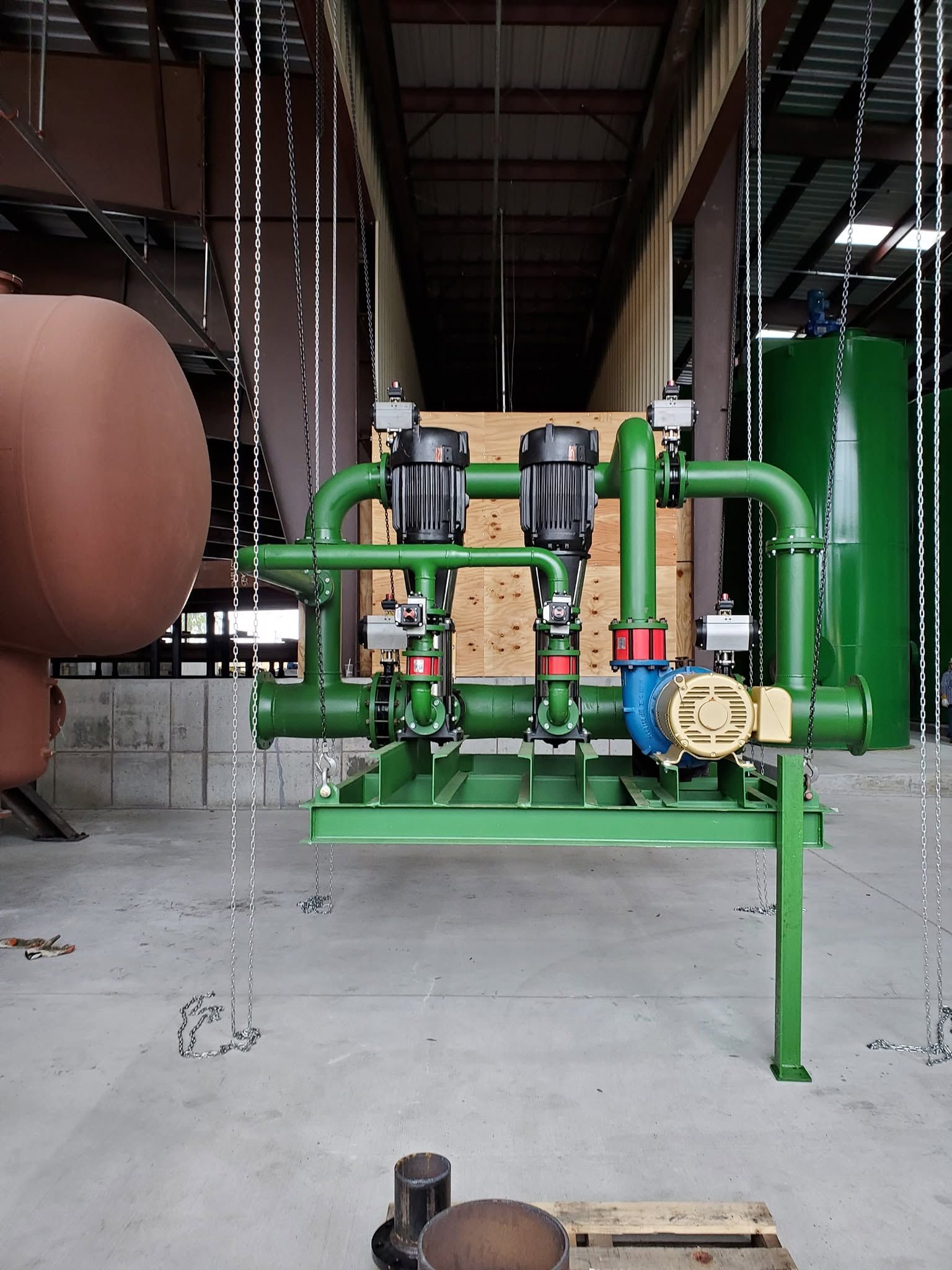Green industrial pump assembly with gauges and pipes in a warehouse workshop