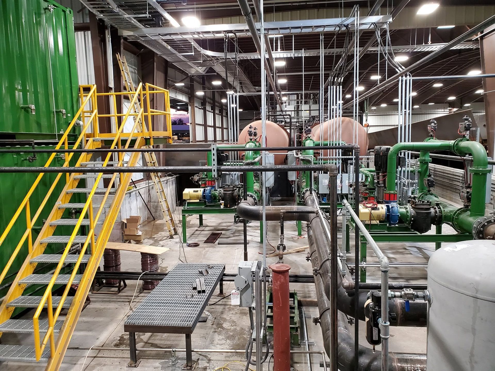 Industrial plant interior with yellow stairs, green pipes, tanks, and metal equipment