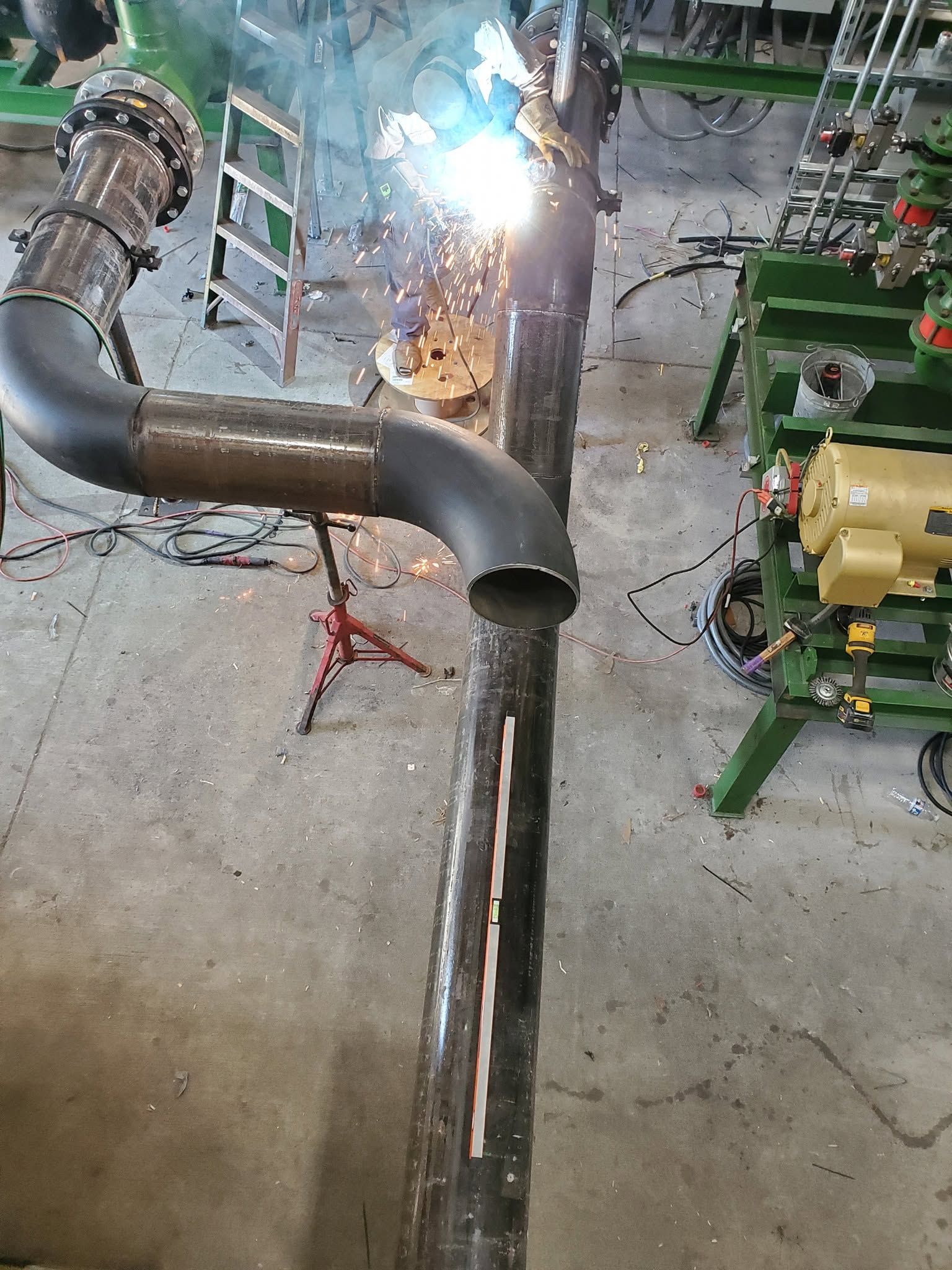Industrial pipe welding in progress, with bright sparks on a metal assembly in a workshop.