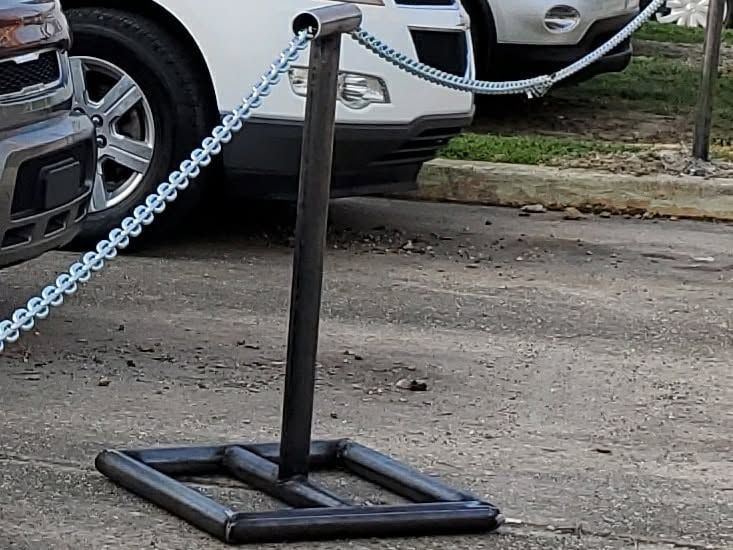 Black metal chain barrier post on a sidewalk beside parked cars and a curb