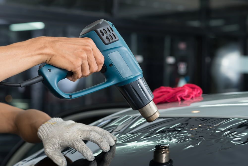 A Man Using Heat Gun On Tint Film — Staunch Window Tinting In Casino, NSW