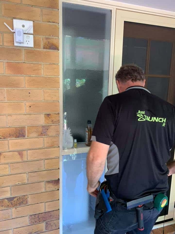 A Man In A Black Shirt Is Standing In Front Of A Brick Wall — Staunch Window Tinting In South Lismore, NSW