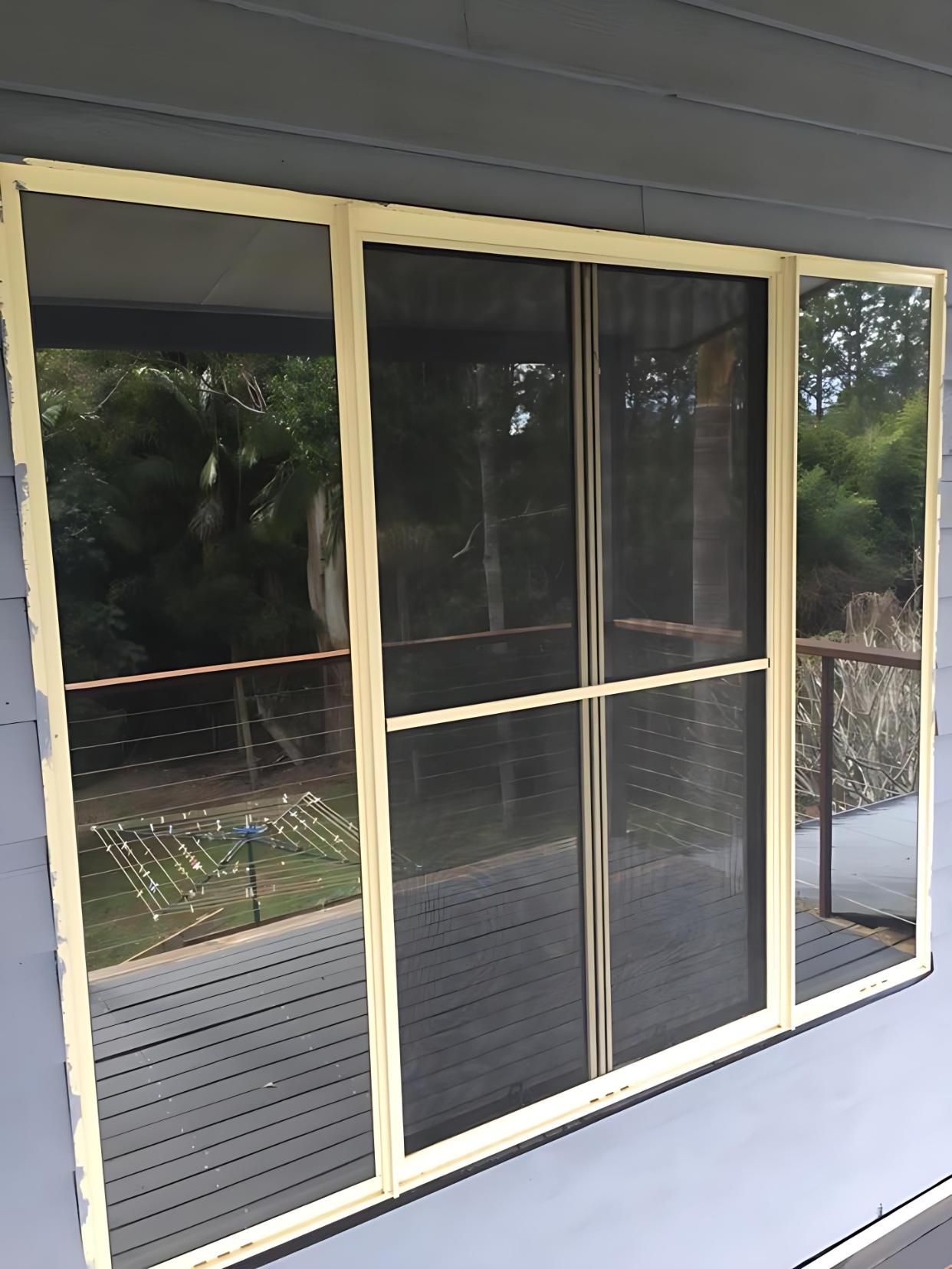 Sliding glass door with a dark reflective tint, reflecting a timber deck and trees, from a completed window tinting Ballina job.