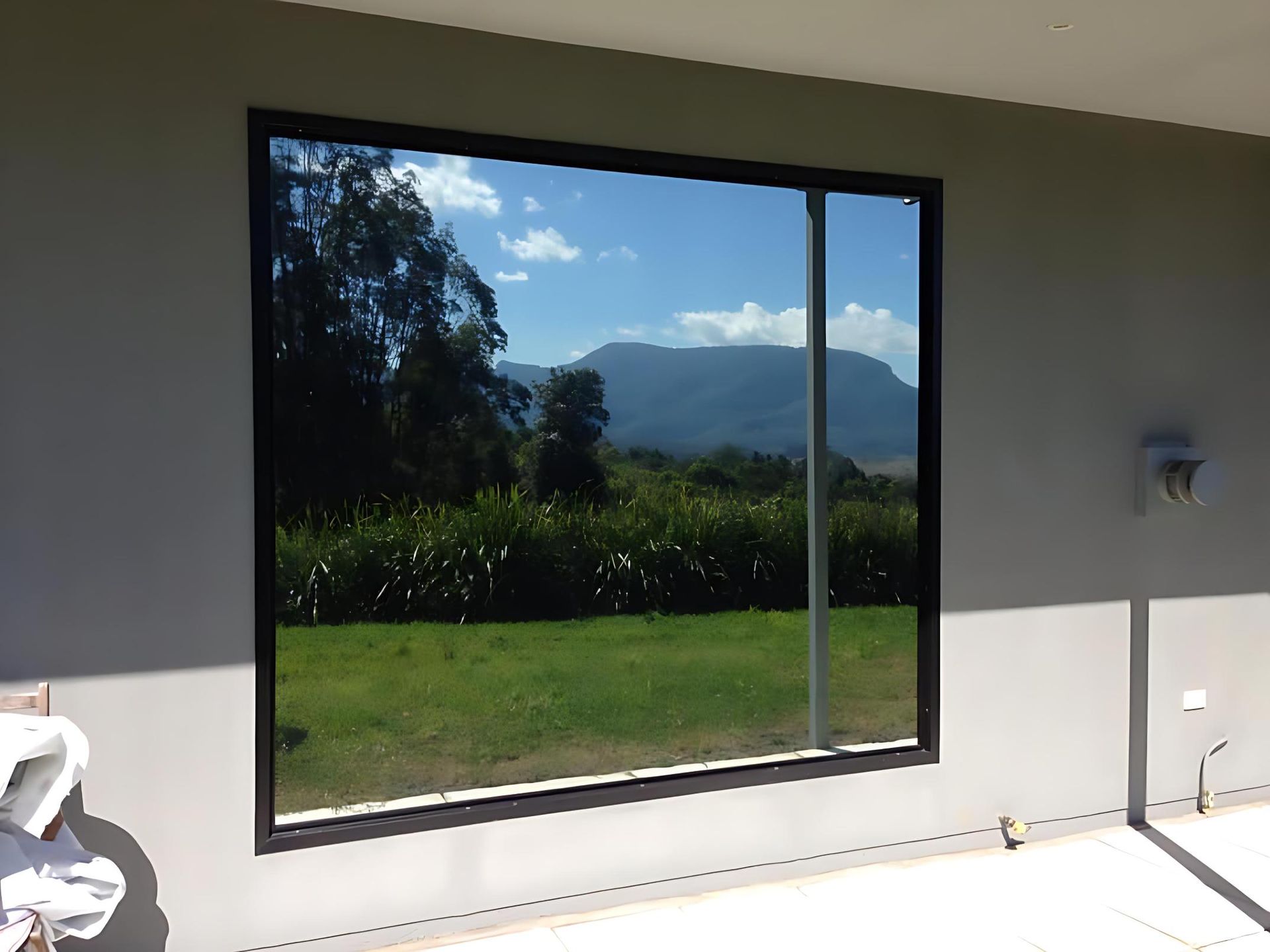 A large tinted window framing a scenic mountain and cane field view, showcasing residential window tinting in Ballina.