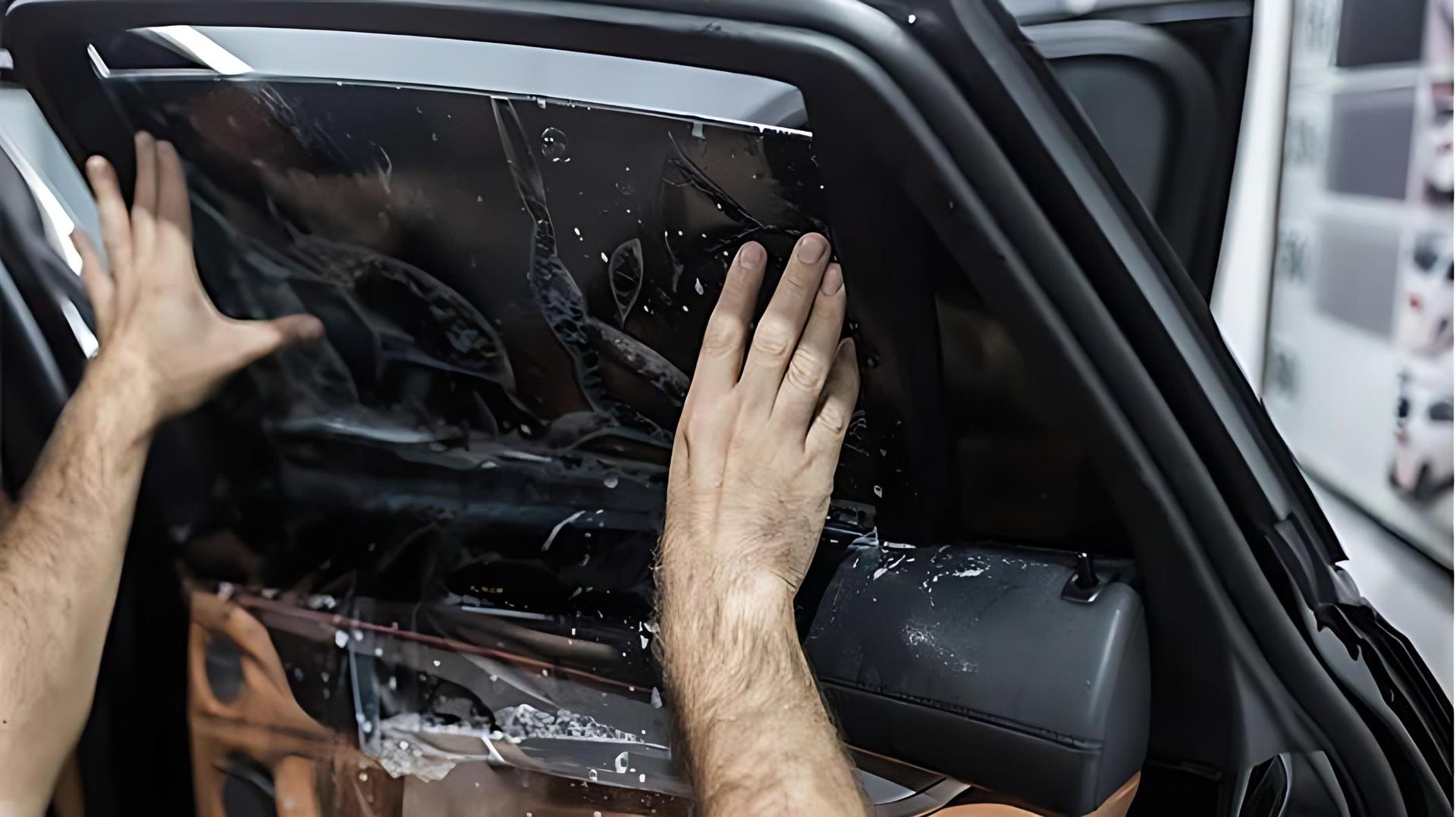 A hand smoothing a car window tint film with soapy water to remove air bubbles, a common process for window tinting in Ballina.