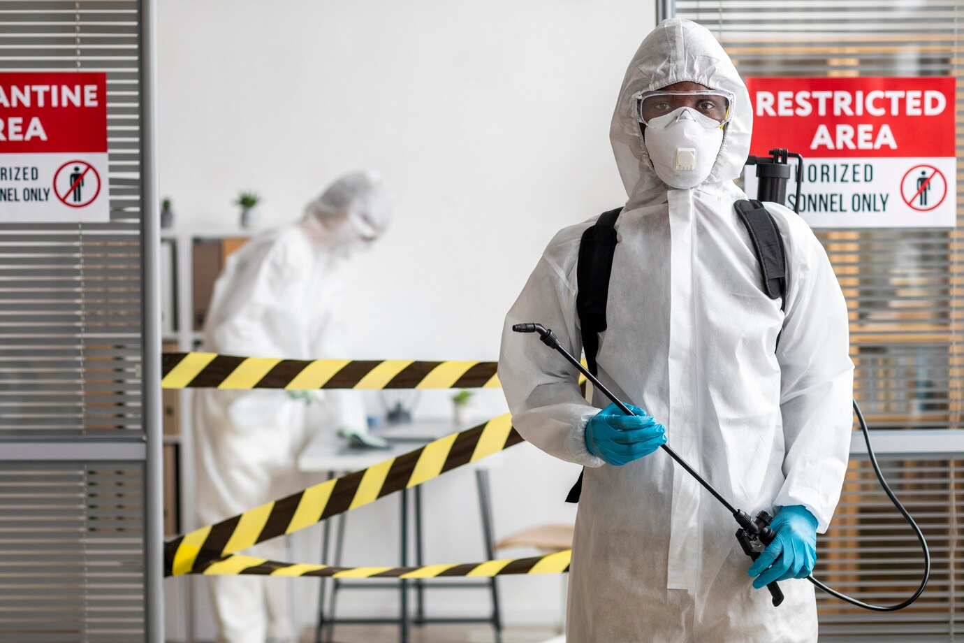 A man in a protective suit is spraying a room with a sprayer.