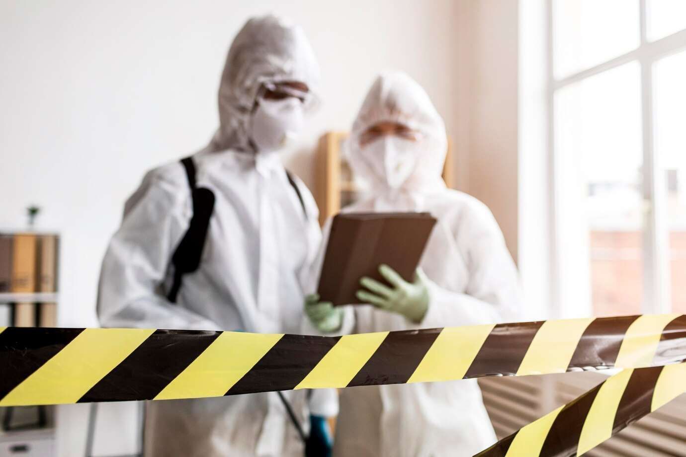 Two people in protective suits are standing next to a yellow and black tape.
