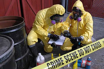 Two men in protective suits are looking at a clipboard next to a crime scene do not cross tape.