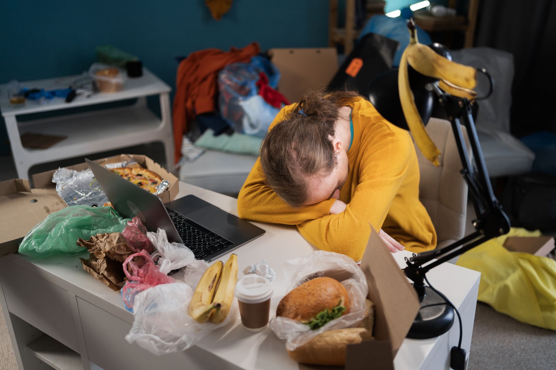 A man is sleeping at a table with food and a laptop.