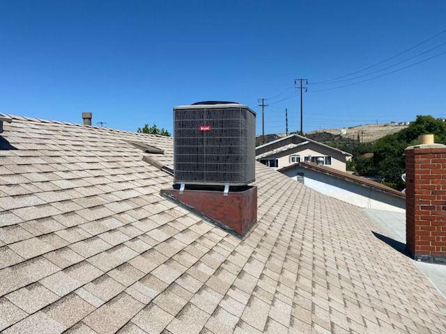 Rooftop HVAC unit on a shingled residential roof under a clear blue sky