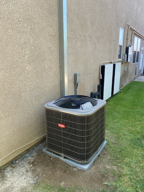Outdoor HVAC unit beside a beige building wall, with green grass and utility piping nearby