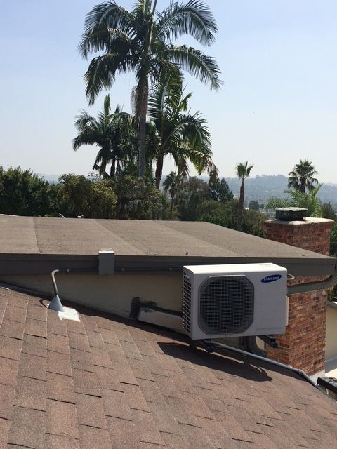 Rooftop air conditioner unit on a sloped shingle roof with palm trees in the background