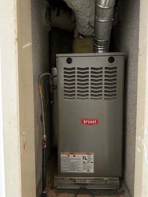 Gray Bryant furnace in a narrow utility closet with exposed ductwork and pipes.