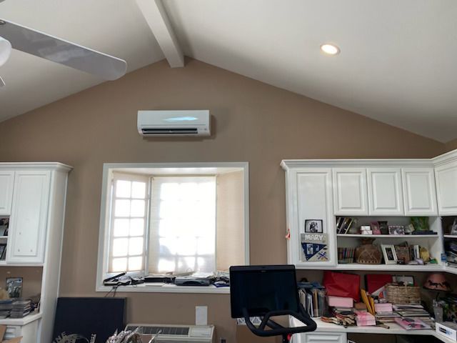 Home office with white cabinets, a window, wall AC unit, and a black office chair
