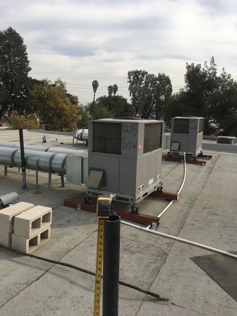 Rooftop HVAC units and large metal pipes on a flat industrial roof under cloudy skies.