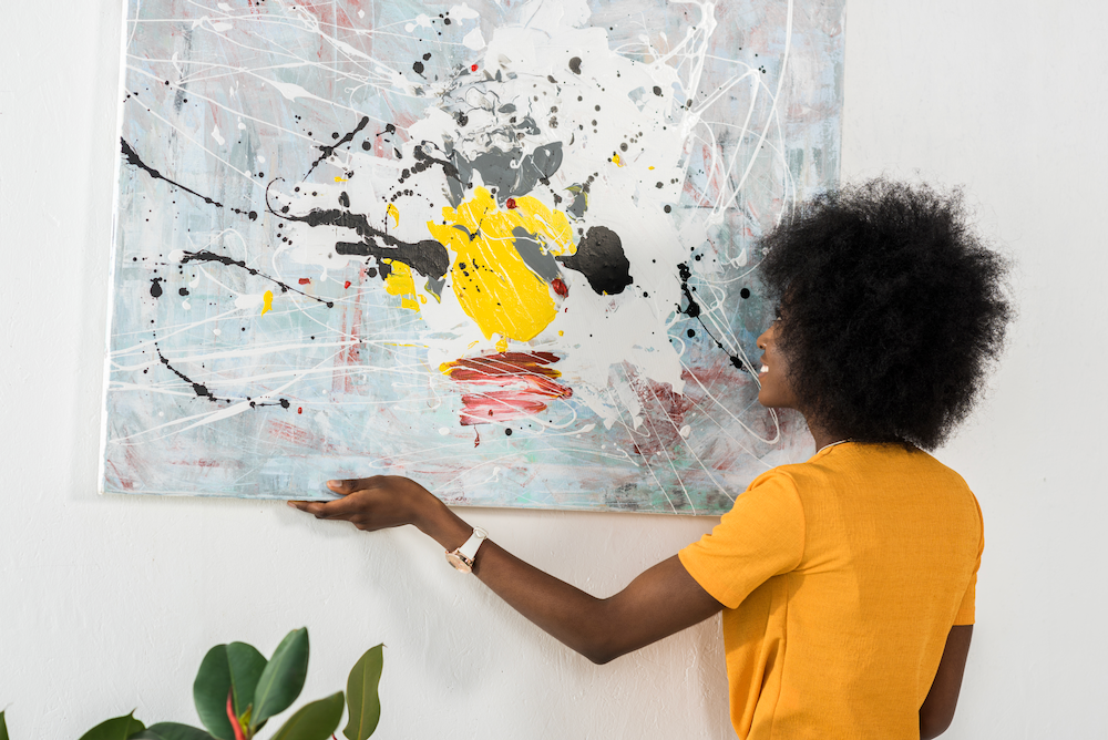A woman is hanging a painting on a wall.