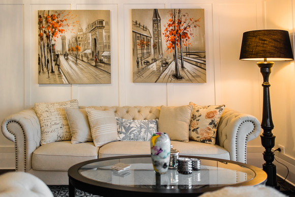 A living room with a couch , coffee table , lamp and three paintings on the wall.