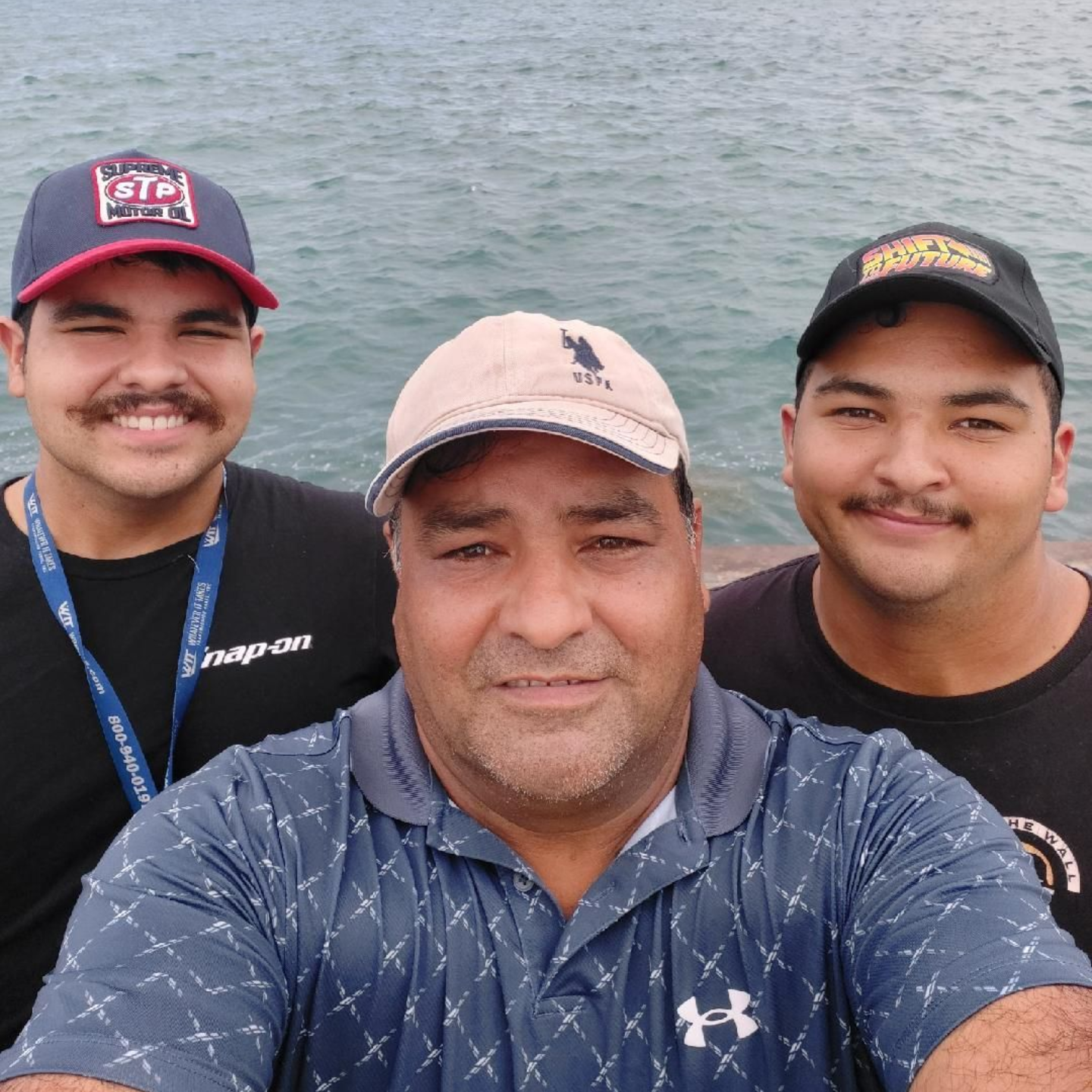 Three people smiling for a selfie on a boat with water and distant shoreline behind them.