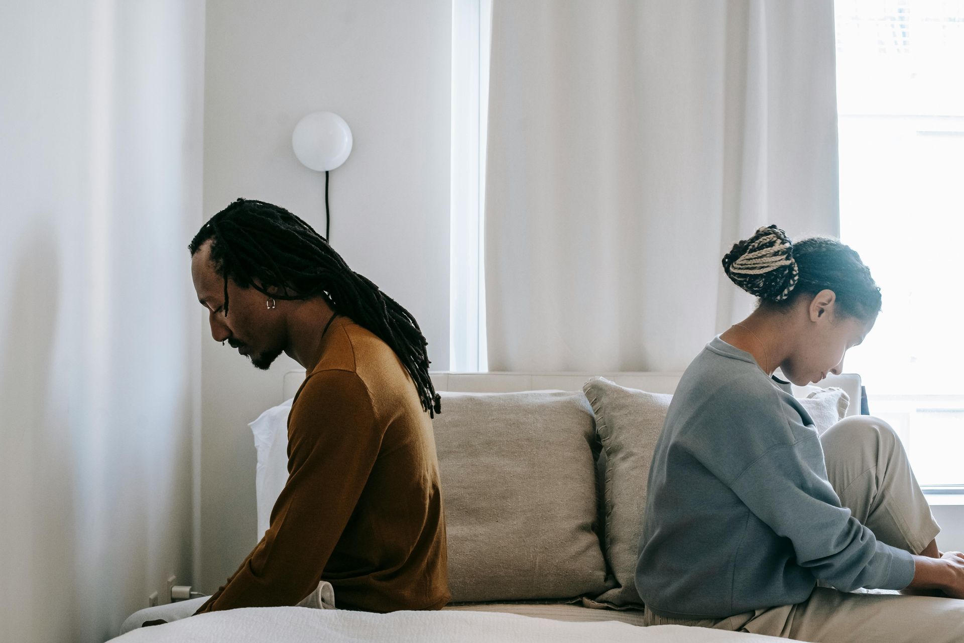 A man and a woman are sitting back to back on a couch.