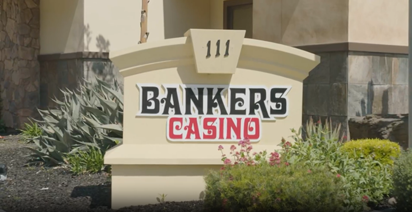 Bankers Casino sign at the entrance of a beige building, with landscaping in front