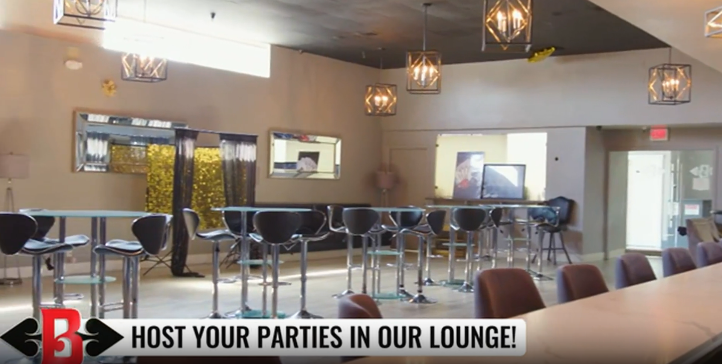 Empty modern lounge with bar stools, pendant lights, mirrors, and a “Host your parties in our lounge!” sign