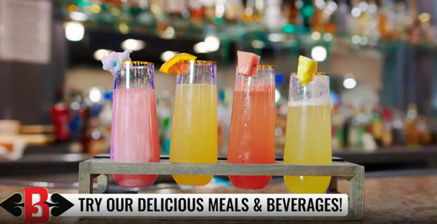 Four colorful cocktails on a bar counter with a “Try our delicious meals & beverages” banner