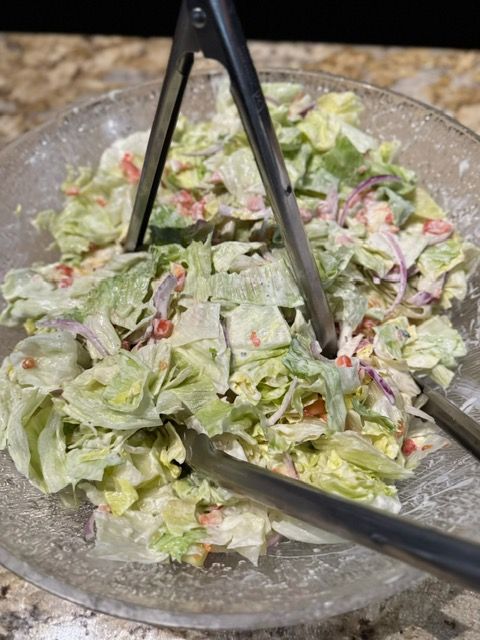 Caesar salad in a glass bowl with black tongs, topped with grated cheese.