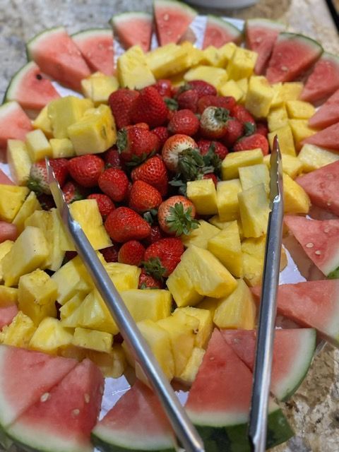 Fruit platter with watermelon border, pineapple chunks, and strawberries, served with tongs