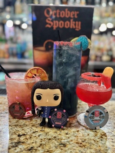 Halloween cocktails with a small figurine and “October Spooky!” sign on a bar counter