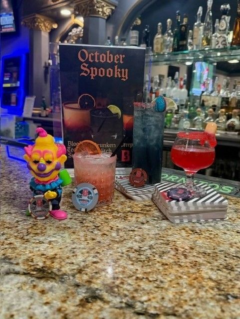 Halloween bar display with spooky cocktails, clown figurine, and an “October Spooky” sign on a granite counter