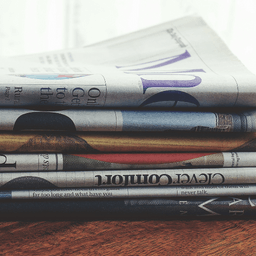 A stack of newspapers sitting on top of each other on a wooden table.