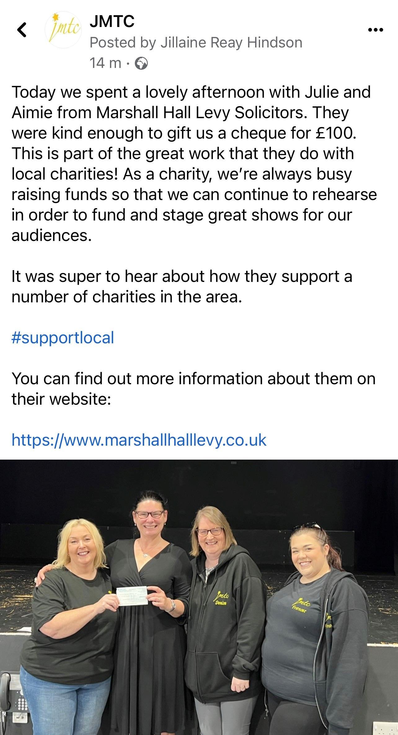 Four women holding a check. One presents it to the others. All smile at the camera.