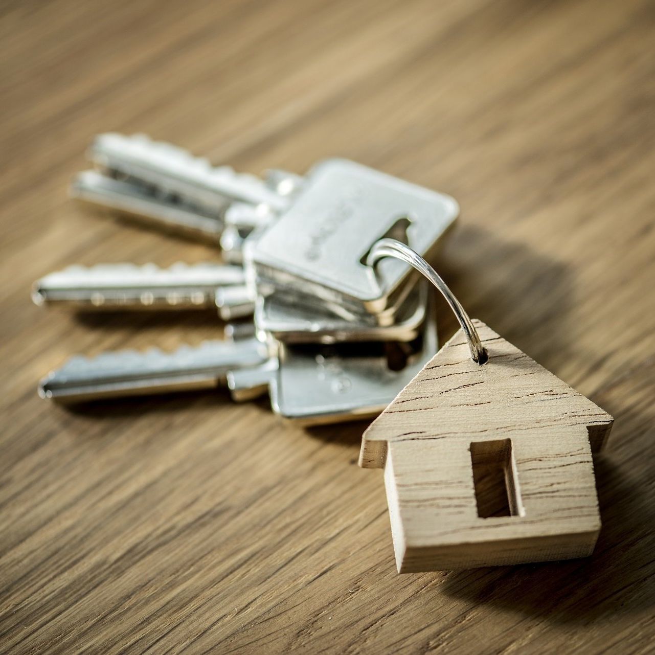 Keys on a wooden surface with a wooden house-shaped keychain.