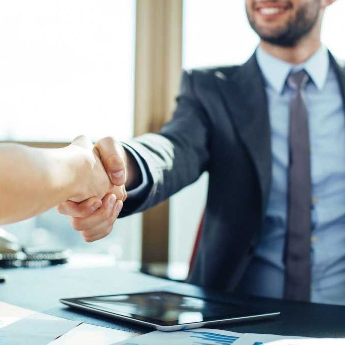 Man in suit shaking hands across a desk with a smiling expression.
