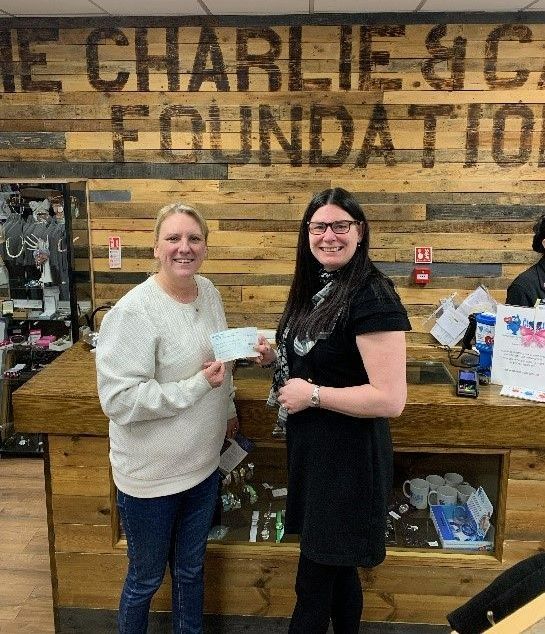Two women at a counter, one holding a check. Behind them, a sign reads 