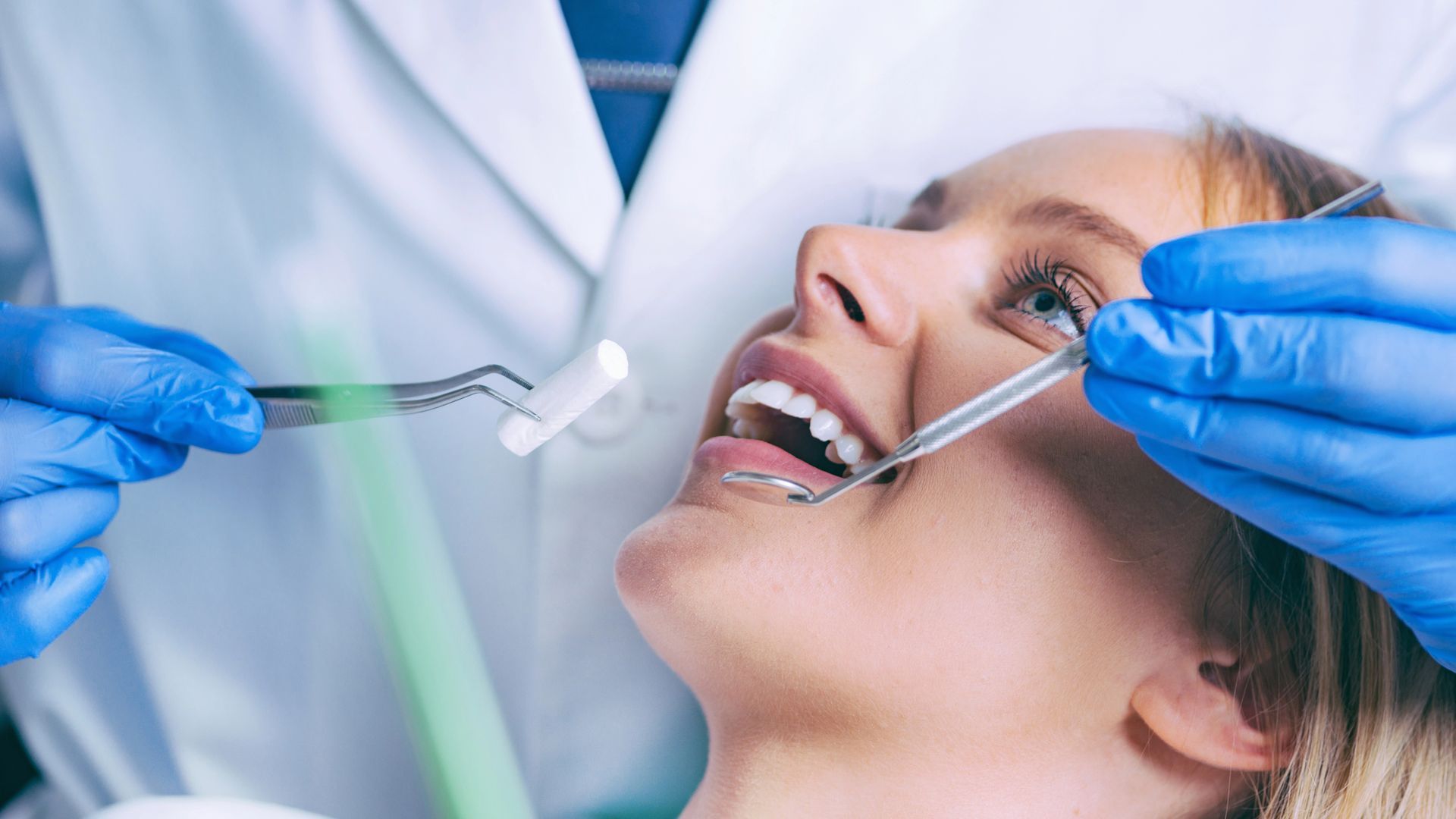 Un dentista in camice bianco esamina i denti di un paziente seduto su una poltrona con l'apparecchio ortodontico.