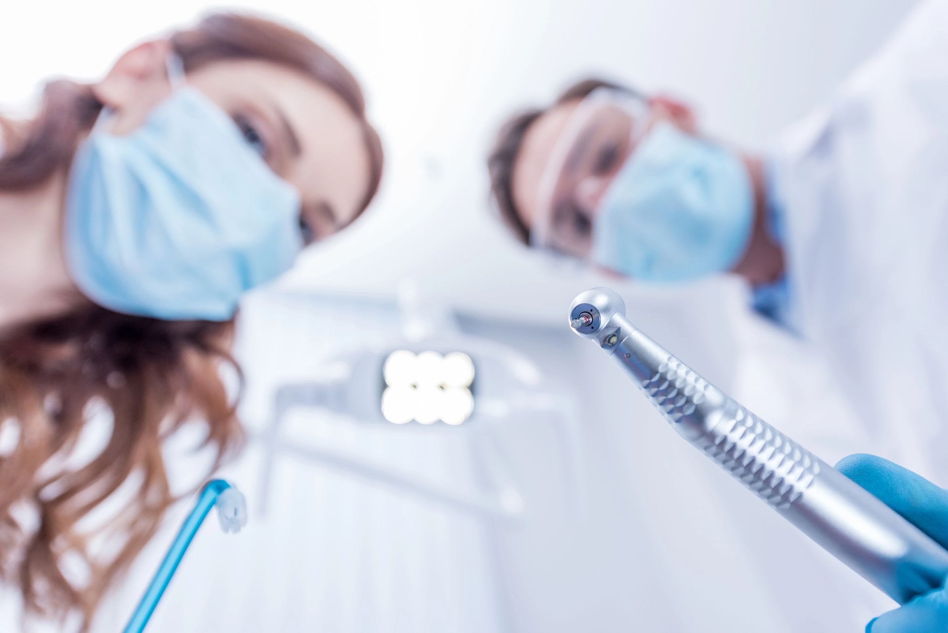 Un dentista con indosso guanti medici blu utilizza un manipolo e uno specchietto dentale per eseguire una visita di controllo di routine su un paziente.