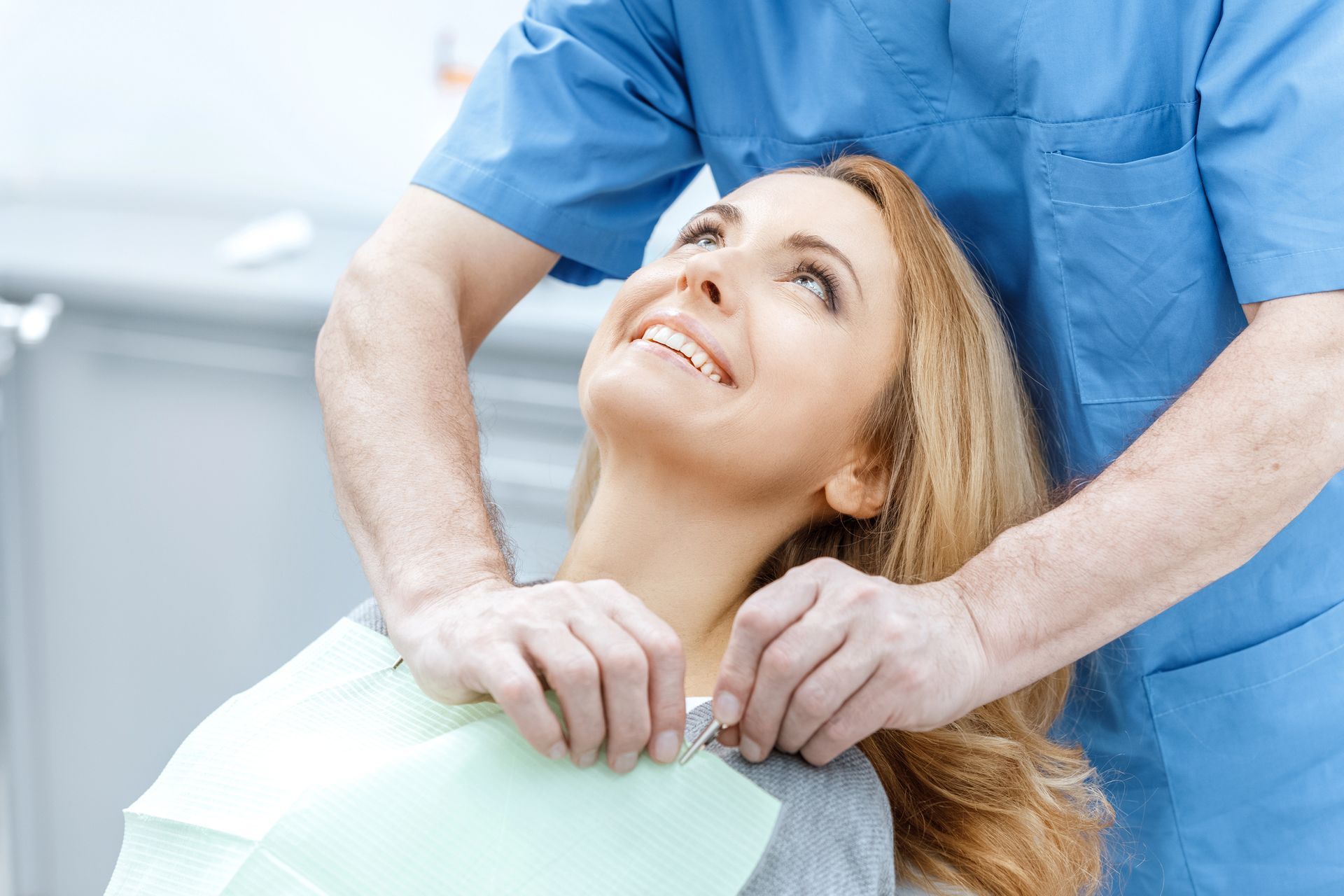 Un dentista sistema il bavaglino di una donna che sorride in una luminosa stanza della clinica.