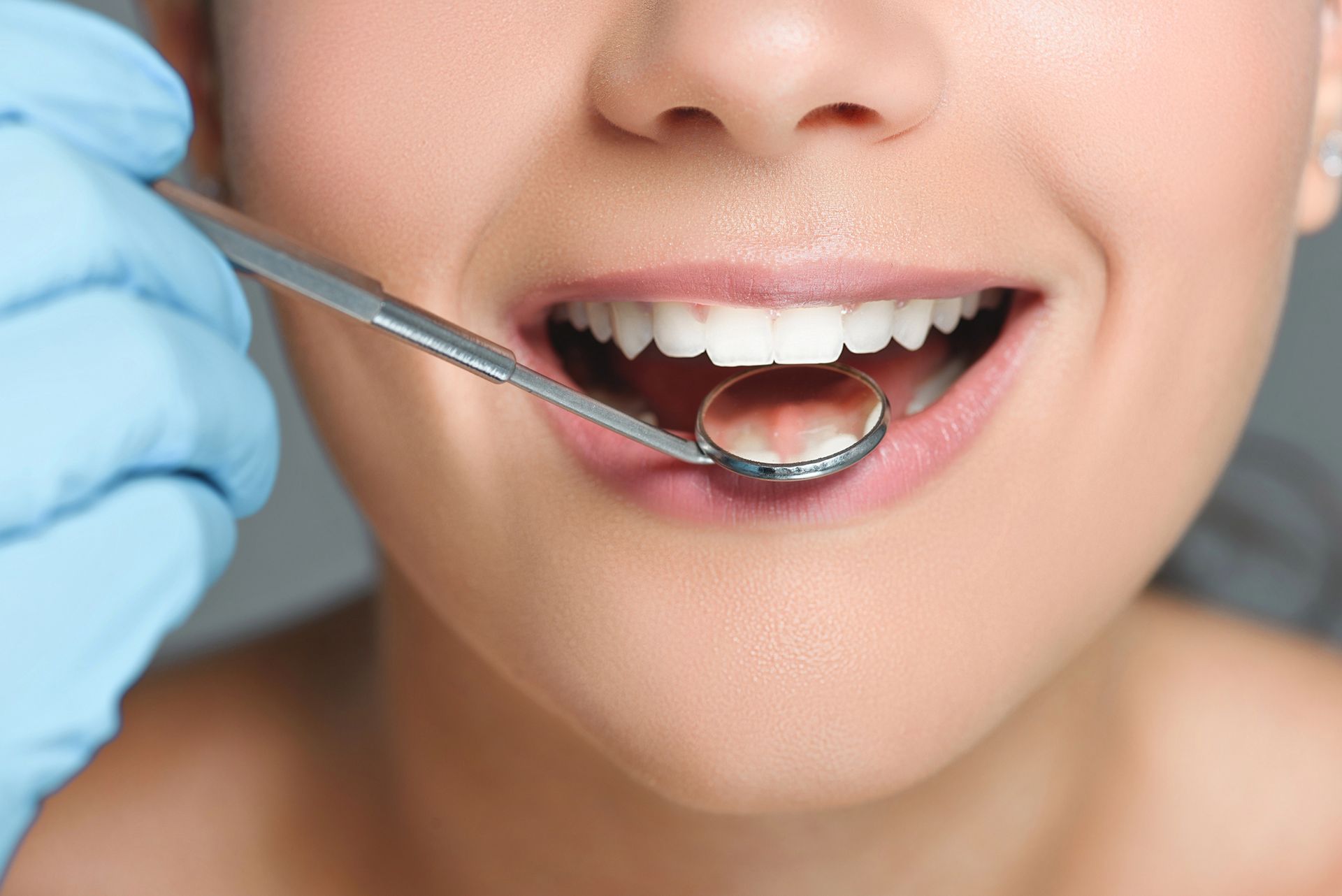 Un dentista esamina la bocca di un paziente sorridente con uno specchietto dentale.