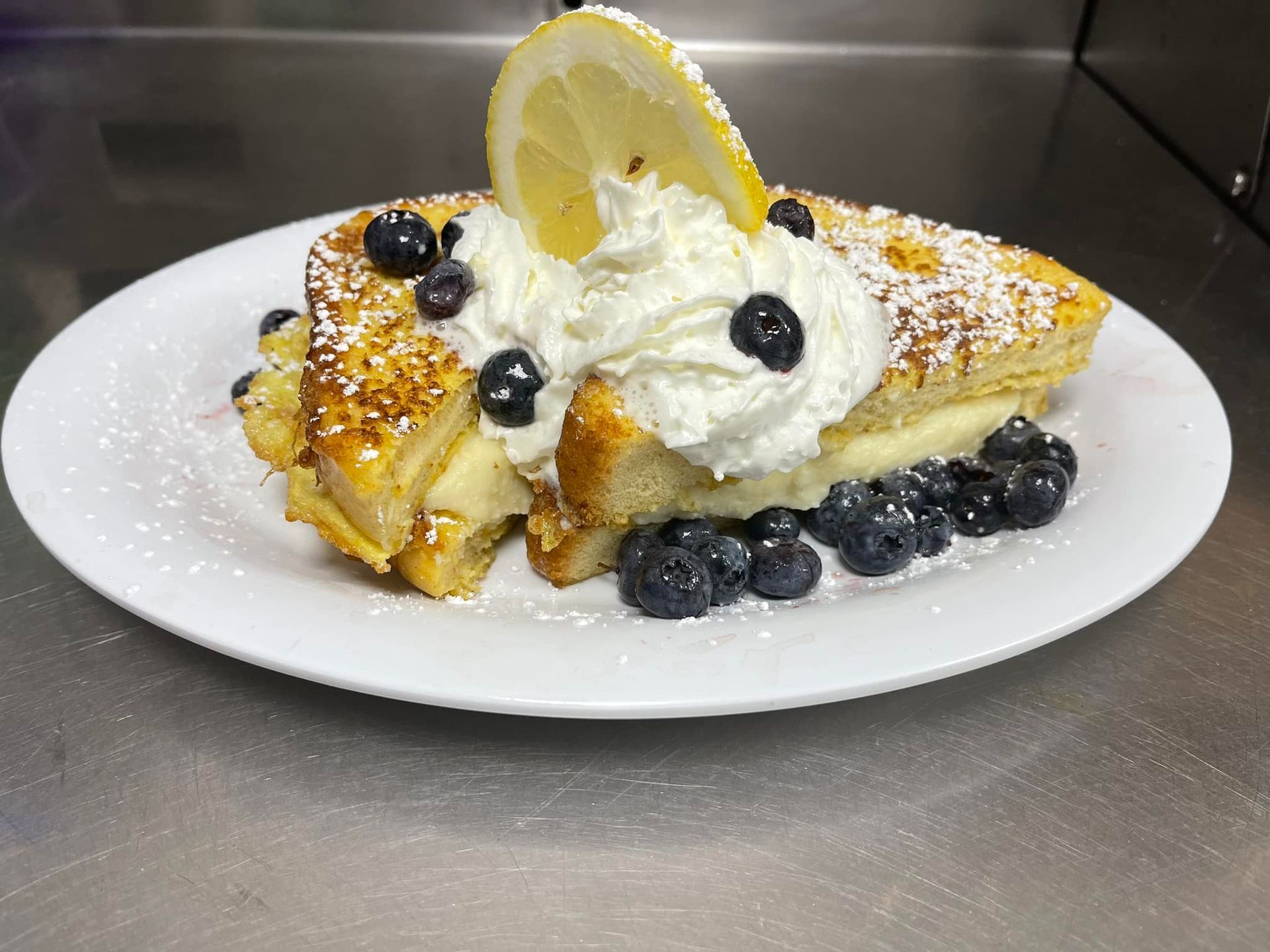 A white plate topped with french toast , blueberries , whipped cream and a lemon slice.
